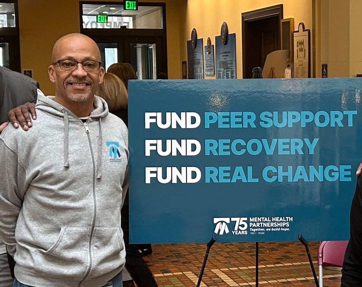 A photo of doc, standing with a sign at advocacy day, supporting the funding of peers support specialists.